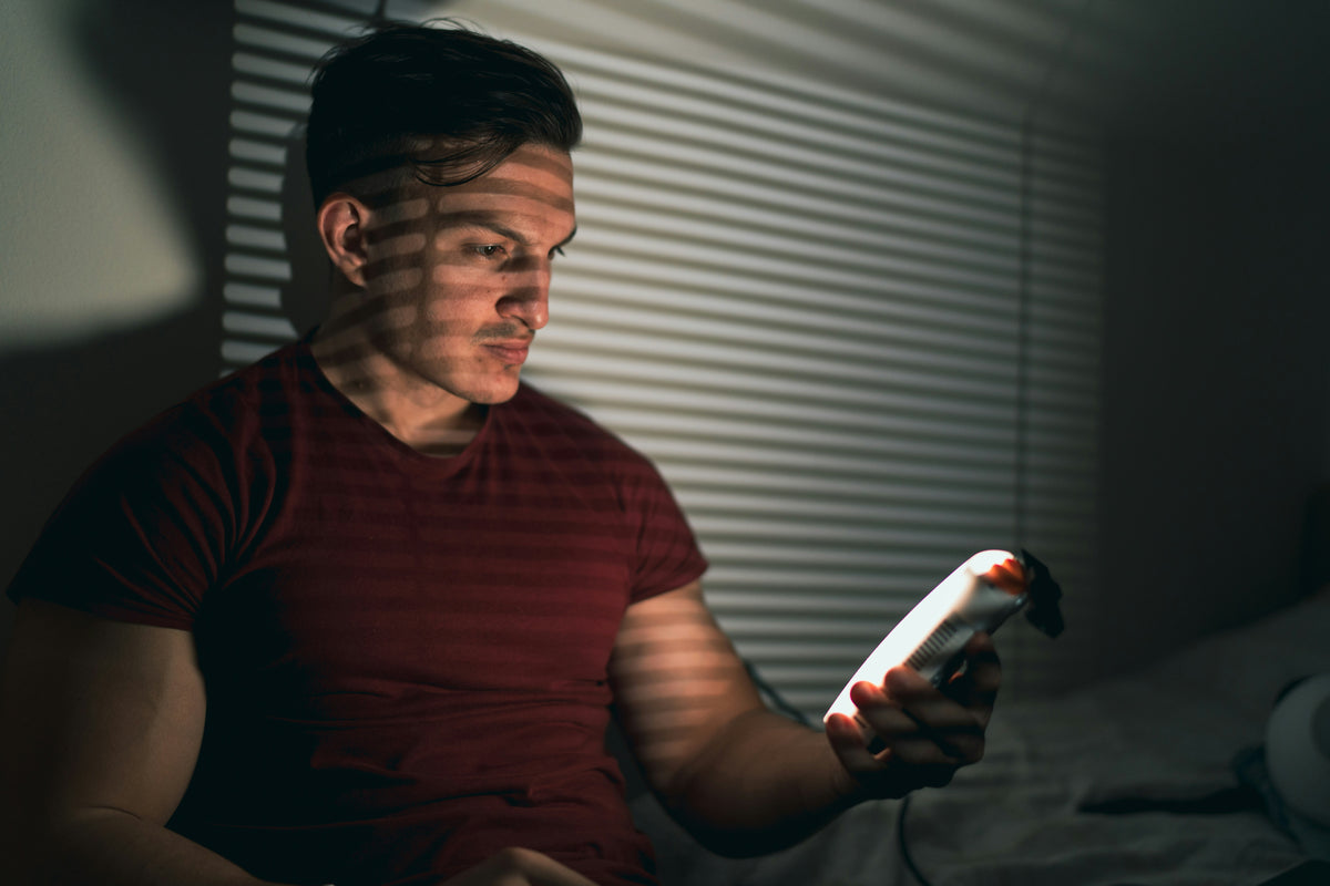 Someone lying in bed at night, lit only by the phone they are scrolling